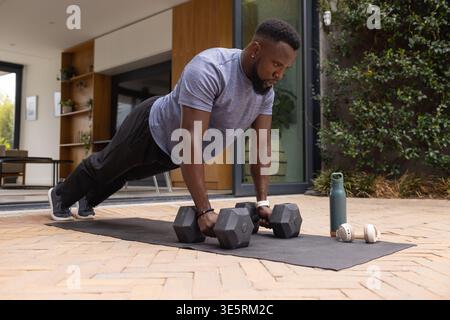 Uomo africano adulto che esegue la tavola usando manichini esagonali sul tappetino del patio mentre indossa una t-shirt grigia Foto Stock