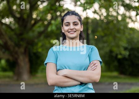 Giovane donna in piedi con sicurezza con le braccia incrociate, sorridente alla macchina fotografica, indossa abbigliamento atletico all'aperto, incarna salute, benessere, e un acti Foto Stock