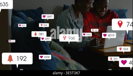 Coppia sorridente che indossa una giacca in denim, camicia rossa che utilizza il computer portatile sul divano del soggiorno e mostra icone Foto Stock