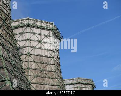Torri di raffreddamento industriali con ponteggi in metallo verde e rivestimento in legno contro un cielo blu. Vista ad angolo basso dell'architetto della stazione di raffreddamento dell'impianto elettrico Foto Stock