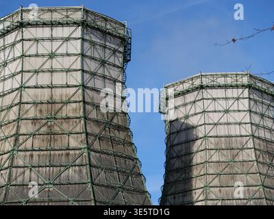 Torri di raffreddamento industriali con ponteggi in metallo verde e rivestimento in legno contro un cielo blu. Vista ad angolo basso dell'architetto della stazione di raffreddamento dell'impianto elettrico Foto Stock
