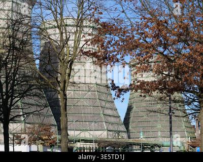 Torri di raffreddamento industriali con ponteggi in metallo verde e rivestimento in legno contro un cielo blu. Vista ad angolo basso dell'architetto della stazione di raffreddamento dell'impianto elettrico Foto Stock