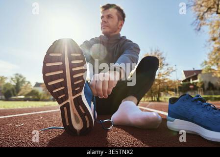 Il runner maschile in sneakers blu si prepara per correre sul circuito dello stadio, da vicino. Le mani maschili si legano alle sneaker sportive per il jogging. Fitness e sana vita Foto Stock