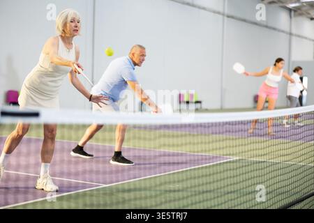 Donna anziana che gioca a pickleball in squadra con partner maschile Foto Stock