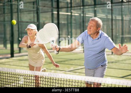 Uomo e donna anziani motivati che giocano a padel con il suo compagno di squadra in tribunale Foto Stock
