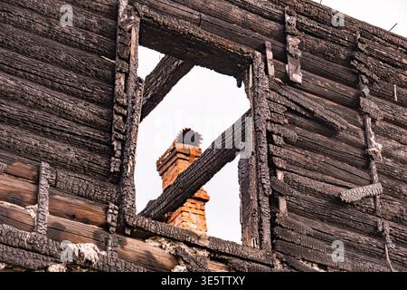 Resti di legno carbonizzato di una casa con una cornice della finestra che rivela un camino in mattoni Foto Stock