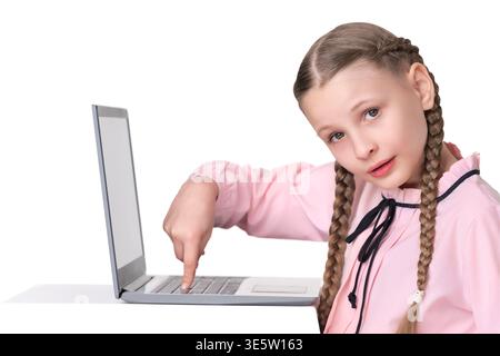 Graziosa studentessa con due trecce in camicetta rosa che punta verso la tastiera del notebook. Bambini che imparano online, fanno i compiti o studiano. Studio shot isolato o Foto Stock