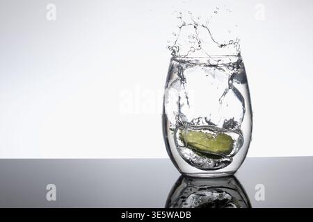 Lime Slice che spruzza nel bicchiere d'acqua con Dynamic Splash su sfondo bianco e Copy Space Foto Stock