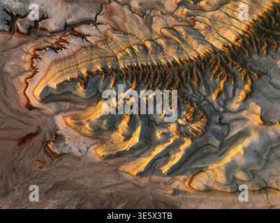 Vista aerea dei canyon testurizzati e degli altipiani a strati immersi nel caldo bagliore del sole che tramonta, creando un netto contrasto con le ombre, Almaty, K. Foto Stock