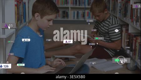 Due ragazzi seduti a lavorare su un computer portatile e un tablet nel corridoio della biblioteca, con notebook e sovrapposizioni digitali Foto Stock