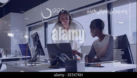 Puntando due colleghi con la parte superiore senza maniche e una camicetta bianca che rivede il laptop in ufficio, sovrapposizioni HUD Foto Stock