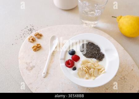 Colazione salutare con yogurt semi di chia e frutti di bosco freschi in ciotola bianca su vassoio di marmo La ripresa ad angolo alto include budino di chia limone e noci Foto Stock