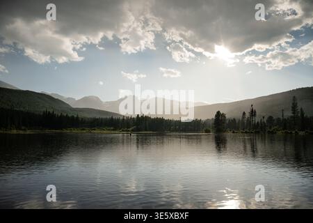 Il sole nebbioso splende sulle montagne e su un lago tranquillo nelle Montagne Rocciose Foto Stock