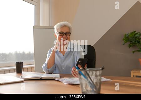 Sicura donna anziana di mezza età euforica vincitrice con smartphone. Signora più anziana matura guardando il telefono delle cellule che legge le notizie grandi ottenendo il buon risultato che vince la sensibilità in linea dell'offerta stupita. Gesto vincente Foto Stock