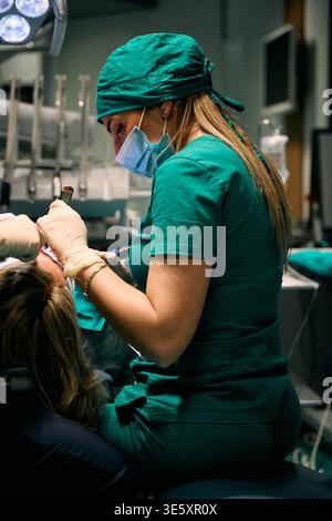 Dentista donna in scrub verdi che cura un paziente durante una procedura odontoiatrica in clinica Foto Stock