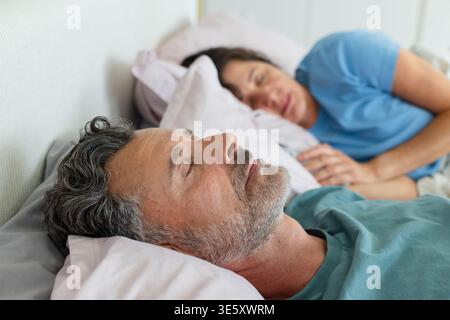 Coppia senior che riposa fianco a fianco sul letto in camera da letto con cuscini, piumone e T-shirt Foto Stock