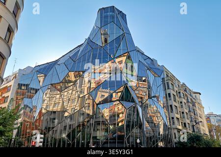 Un edificio moderno sorge a Bilbao, in Spagna. Il suo design unico riflette le strutture vicine in una giornata limpida. La gente passeggia e ammira il panorama. Foto Stock