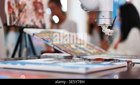 Primo piano di un braccio robot IA che dipinge un quadro astratto su tela in uno studio d'arte Foto Stock