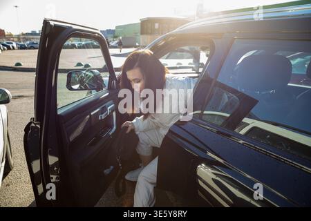 Donna che esce dalla sua auto in un parcheggio. Spostamenti giornalieri o viaggi per adulti o giovani. Concetto di proprietà automobilistica. Foto Stock