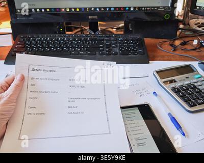 Kirov, Russia - 18 marzo 2026: Una persona esamina i dettagli del pagamento delle utenze e calcola le spese della famiglia a una scrivania con computer e documenti. Foto Stock