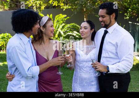 Sposa in abito da sposa, sposo in cravatta nera e due ospiti che si divertono a bere champagne nel cortile Foto Stock