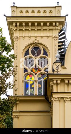 Facciata ornata di un edificio storico con vetrate ad arco, colonne decorative e cornice, vista contro il cielo coperto con rami di alberi e un m Foto Stock