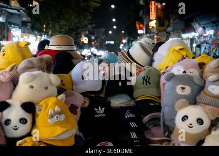 Hanoi, Vietnam - febbraio 2026: Venditore ambulante che vende cappelli e peluche in un mercato notturno frenetico della città Foto Stock