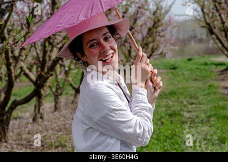 Donna sorridente mentre tiene in mano un ombrellone rosa nel frutteto Foto Stock