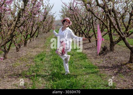 Donna che balla felicemente in un campo di pesca fiorito Foto Stock