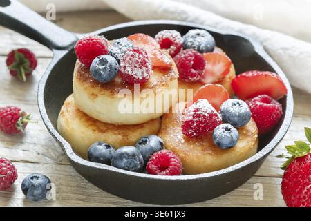 Cottage cheese pancakes, syrniki, frittelle di cagliata con frutti di bosco freschi (lampone, fragola, mirtillo, mora) e zucchero in polvere in una ghisa pa Foto Stock