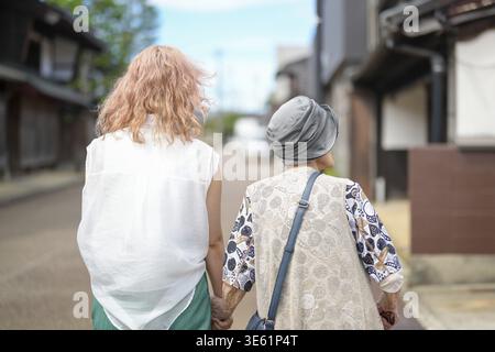 Due donne che camminano per strada, una di loro indossa una camicia bianca. La donna con la camicia bianca tiene la mano della donna nel gilet grigio Foto Stock