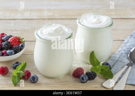 Cibo, yogurt greco fresco in vaso di vetro servito con bacche miste, sana colazione, sfondo in legno Foto Stock