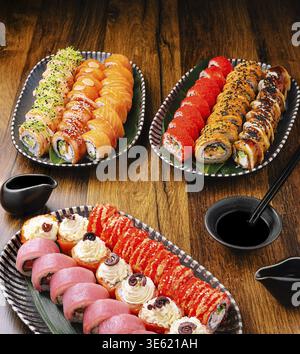 Cibo, piatti colorati di sushi pieni di vari tipi di panini sono presentati su un tavolo di legno. La salsa di soia viene collocata nelle vicinanze, migliorando la qualità culinaria Foto Stock