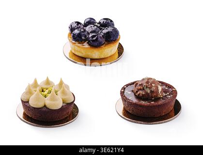 Cibo, tre squisiti mini dessert includono una crostata ai mirtilli, una crostata alla crema di cioccolato e una torta al pistacchio. Ogni dessert è accuratamente presentato su oro ba Foto Stock