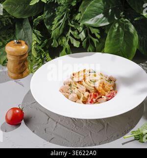 Cibo, deliziose tagliatelle con gamberi, salmone e verdure fresche in salsa cremosa, servite in piatto bianco Foto Stock