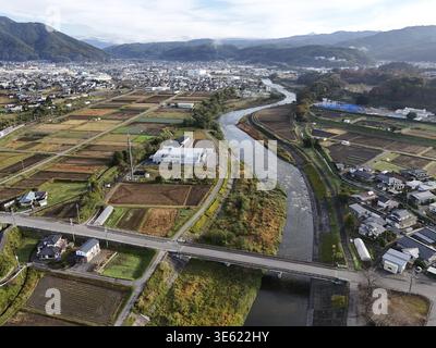 Un'area rurale con un fiume che la attraversa. Il fiume è circondato da terreni agricoli e case. Il cielo è limpido e il sole splende Foto Stock