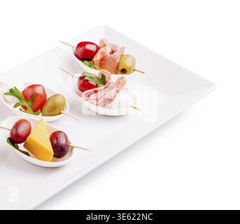 Cibo: Un delizioso assortimento di piccoli antipasti disposti su un piatto bianco. Gli spiedini contengono formaggio, olive, pomodori ciliegini e affettati, perfe Foto Stock