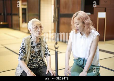 Una donna con i capelli rosa si siede accanto a una donna più anziana. La donna più anziana indossa occhiali e un giubbotto. Le due donne parlano tra loro Foto Stock