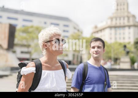 Una donna e un uomo camminano per strada, entrambi con zaini. La donna indossa una camicia bianca e occhiali da sole, mentre l'uomo indossa una blu Foto Stock