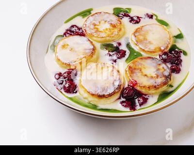 Cibo, frittelle di formaggio casereccio (syrniki) servite con salsa cremosa, condimento di frutti di bosco e guarnigione fresca su un piatto, tradizionale d'Europa orientale Foto Stock