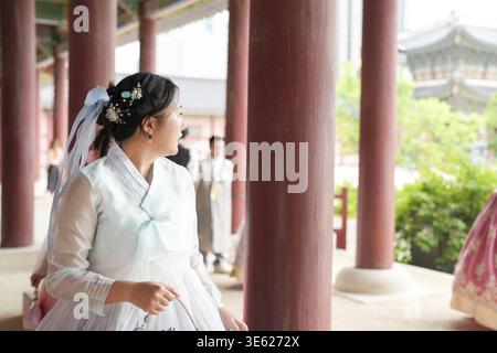A giugno a Seul, due donne coreane sui trent'anni camminano sotto i grandi pilastri di pietra del Palazzo Gyeongbokgung, parlando mentre indossano graziosi rosa e. Foto Stock