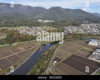 Un'area rurale con un fiume che la attraversa. Il fiume è circondato da terreni agricoli e case. Il cielo è limpido e il sole splende Foto Stock
