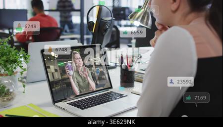 Donna seduta in gilet nero bianco che guarda il laptop che mostra i badge di reazione in ufficio, copia spazio Foto Stock