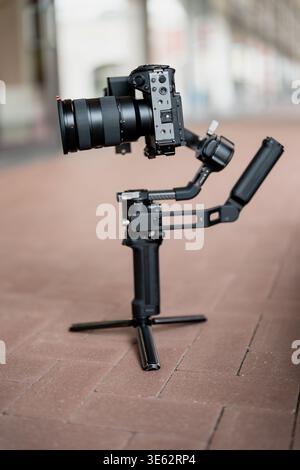 Fotocamera mirrorless con obiettivo zoom montato su treppiede cardanico motorizzato sul pavimento, che mostra apparecchiature per la realizzazione di film portatili per il lavoro e i video dei creatori Foto Stock