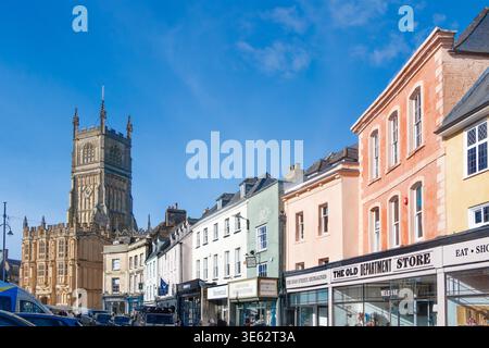 La storica chiesa parrocchiale di Cirencester di St John Baptist e i tradizionali negozi colorati nella piazza del mercato di Cirencester Gloucestershire, Inghilterra Foto Stock