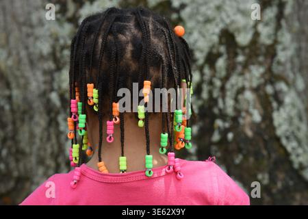 Primo piano sulla schiena di una giovane donna con i capelli intrecciati decorati con perline colorate, una vivace acconciatura africana che simboleggia l'identità culturale e Foto Stock