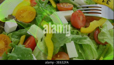 Esposizione dell'insalata sul bancone con lattuga, pomodori, feta, forchetta, nastro giallo, brusio verde Foto Stock