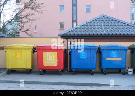 I contenitori di riciclaggio con codice colore sono allineati all'esterno vicino a edifici residenziali per la raccolta e la raccolta dei rifiuti Foto Stock