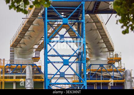 Una visuale ad angolo basso di un grande impianto industriale con un'evidente struttura a capriata in acciaio blu che supporta due massicce strutture cilindriche bianche, Foto Stock