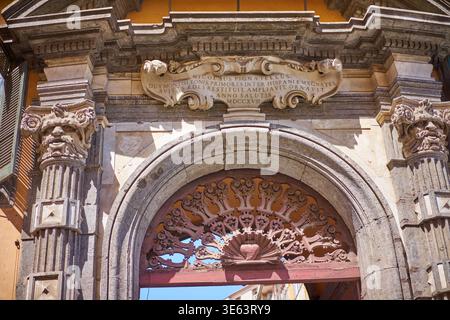 Vista ravvicinata di un portale in pietra barocca ornato su uno storico edificio italiano, caratterizzato da un grande arco arrotondato con cornice in pietra arrugginita Foto Stock